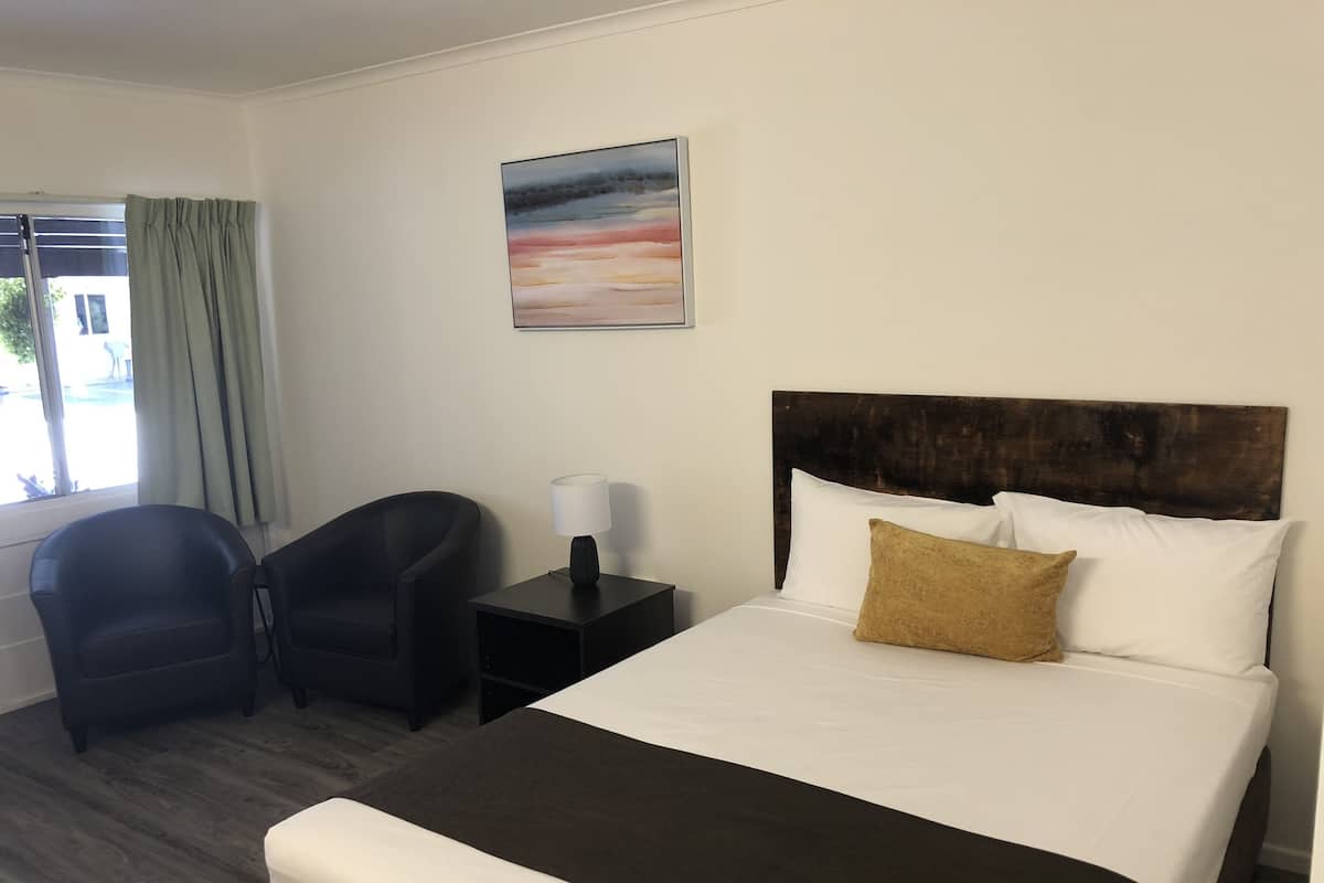 A hotel room with a bed, a chair, a nightstand, a lamp, and a window with curtains.