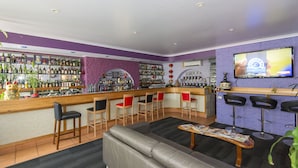 A bar area with a counter, multiple bar stools, a sofa, and a television screen. - Coral Sands Motel (Mackay)