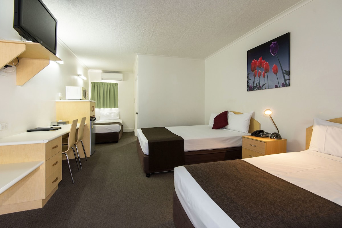 A hotel room with a bed, a desk, a chair, a small table, a bedside lamp, and a painting on the wall.