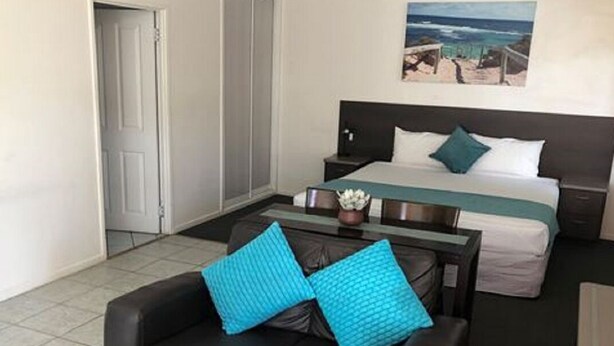 A hotel room with a bed, a desk, a chair, and a painting on the wall. - Coral Sands Motel (Mackay)