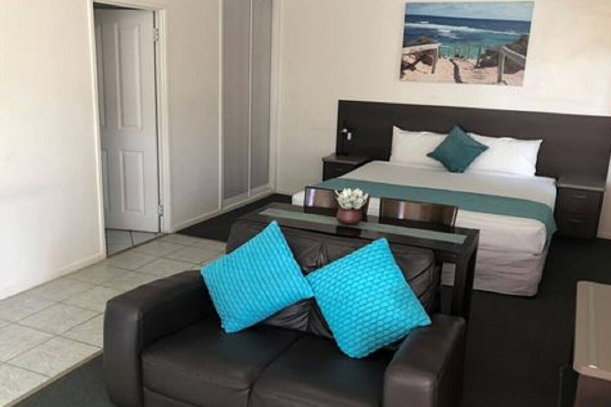 A hotel room with a bed, a desk, a chair, and a painting on the wall.