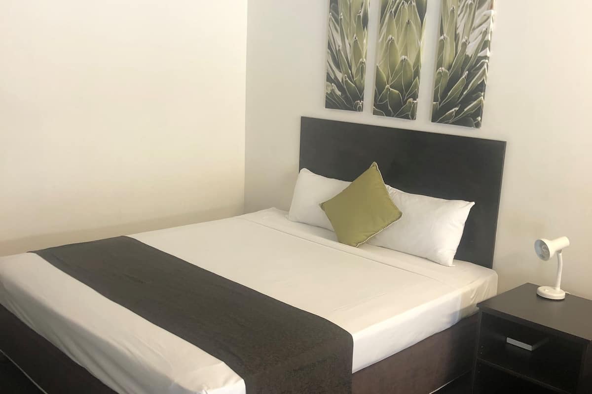A neatly made bed with a dark headboard, white bedding, and a green pillow. There are three wall-mounted artworks above the bed.