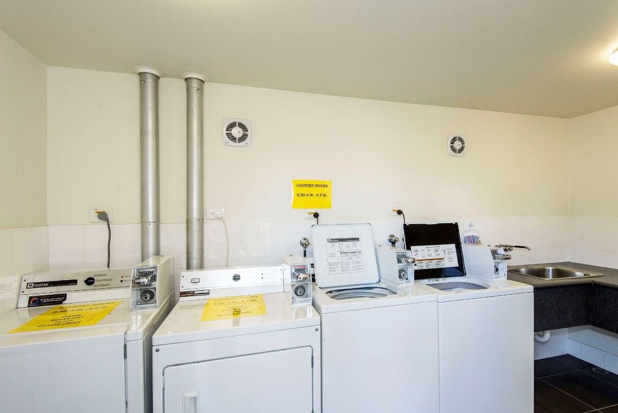 A laundry facility with multiple washing machines, a sign indicating laundry hours, and a sink area.