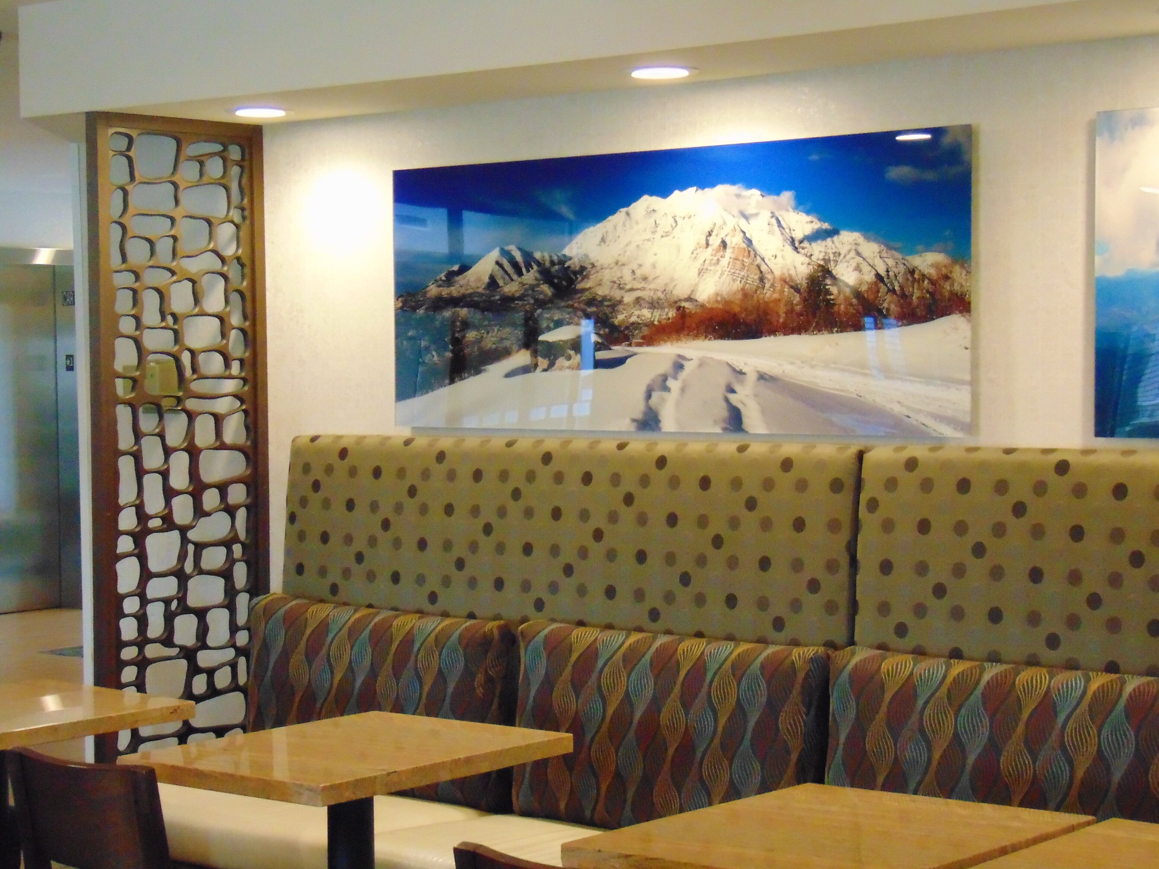 A restaurant interior with a patterned booth seating, a large wall-mounted picture of a mountain, and a decorative partition.