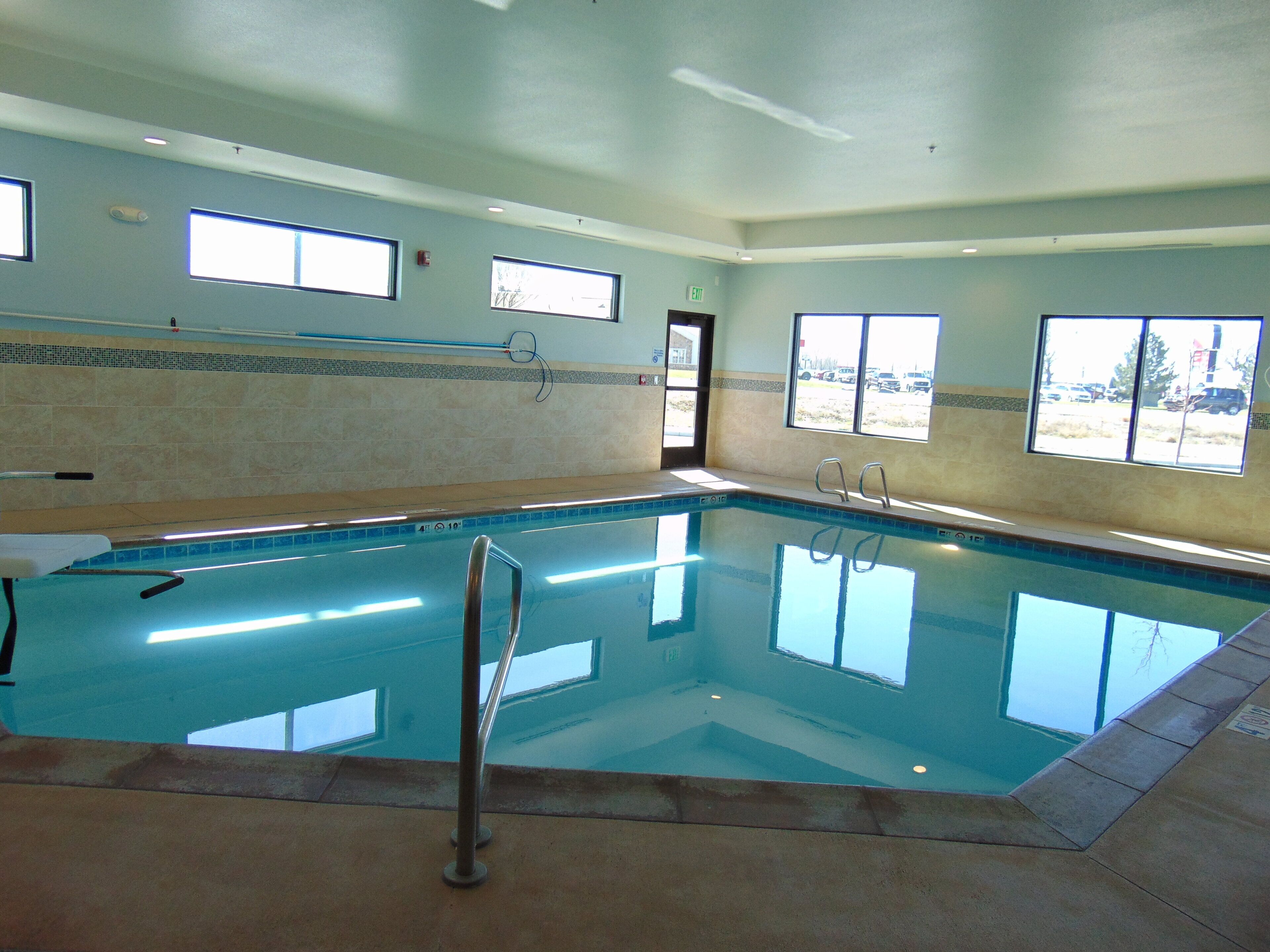 An indoor swimming pool with clear glass walls, a tiled floor, and multiple windows providing natural light.