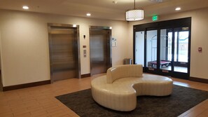 A lobby with two elevators, a waiting area with a curved bench, and a glass door leading outside. - Holiday Inn Express & Suites Springville-South Provo Area by IHG (Springville)