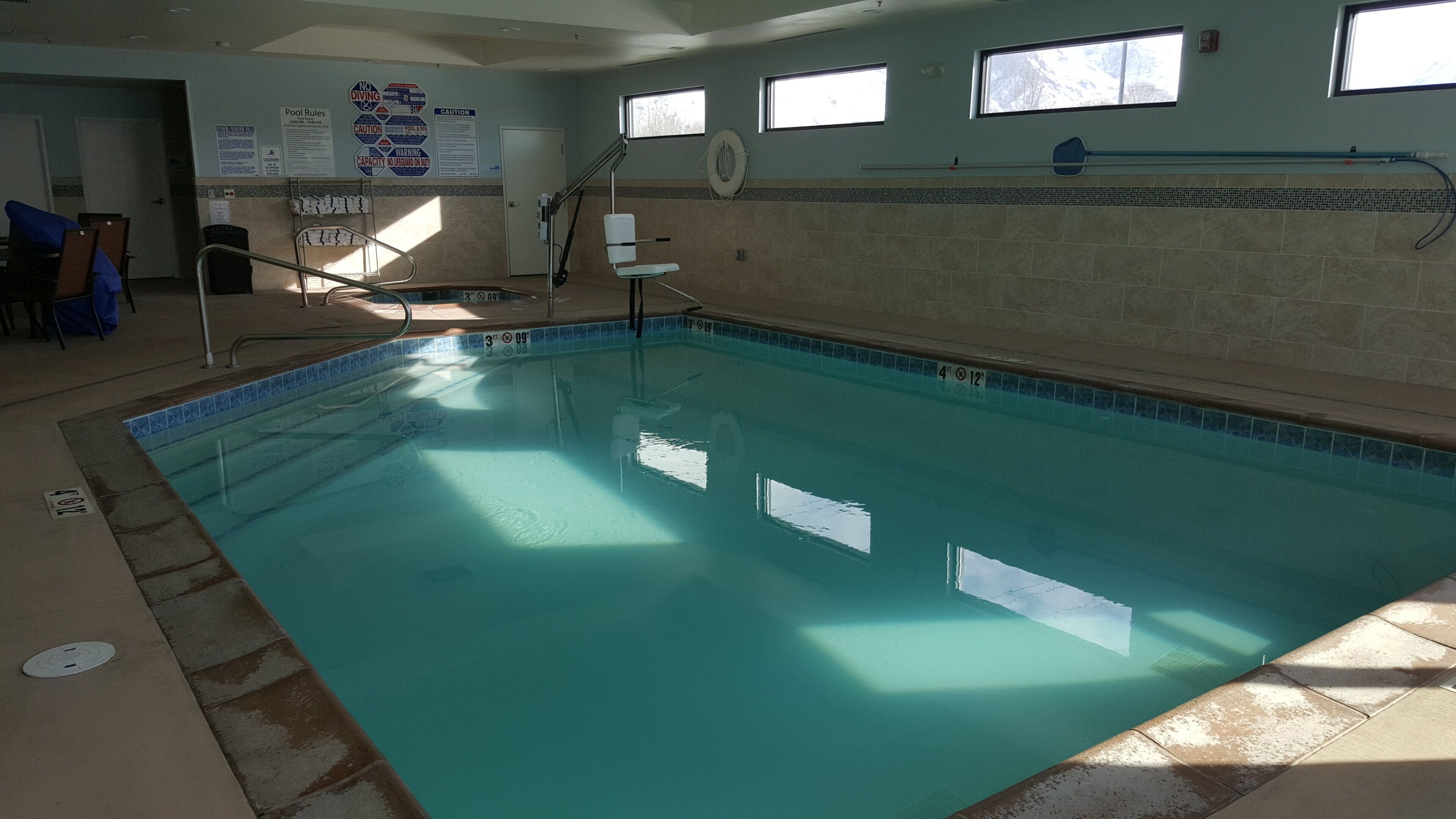 An indoor swimming pool with clear water, a diving board, and safety signs on the walls.
