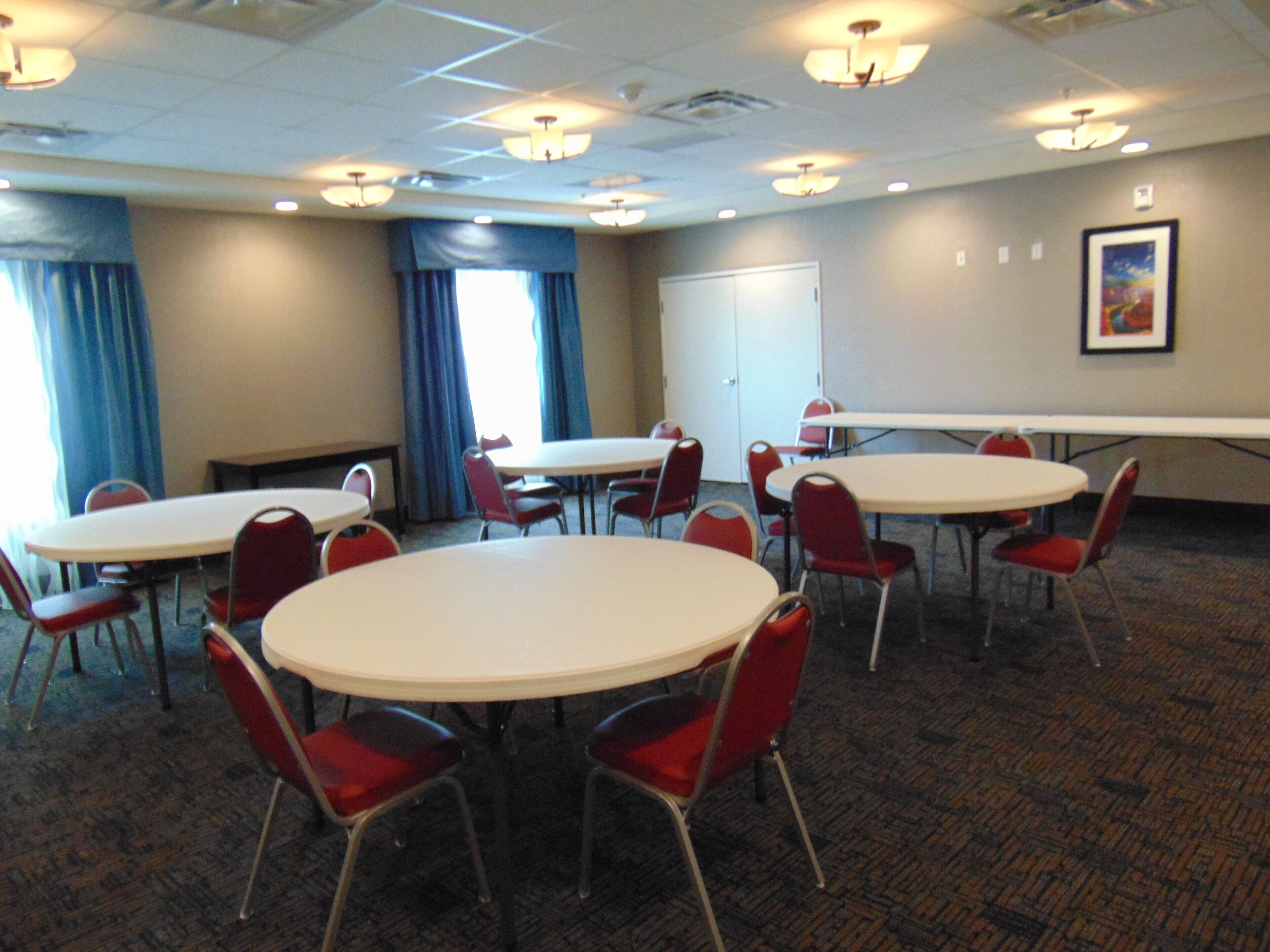 A conference room with round tables and red chairs, a whiteboard, and a door.