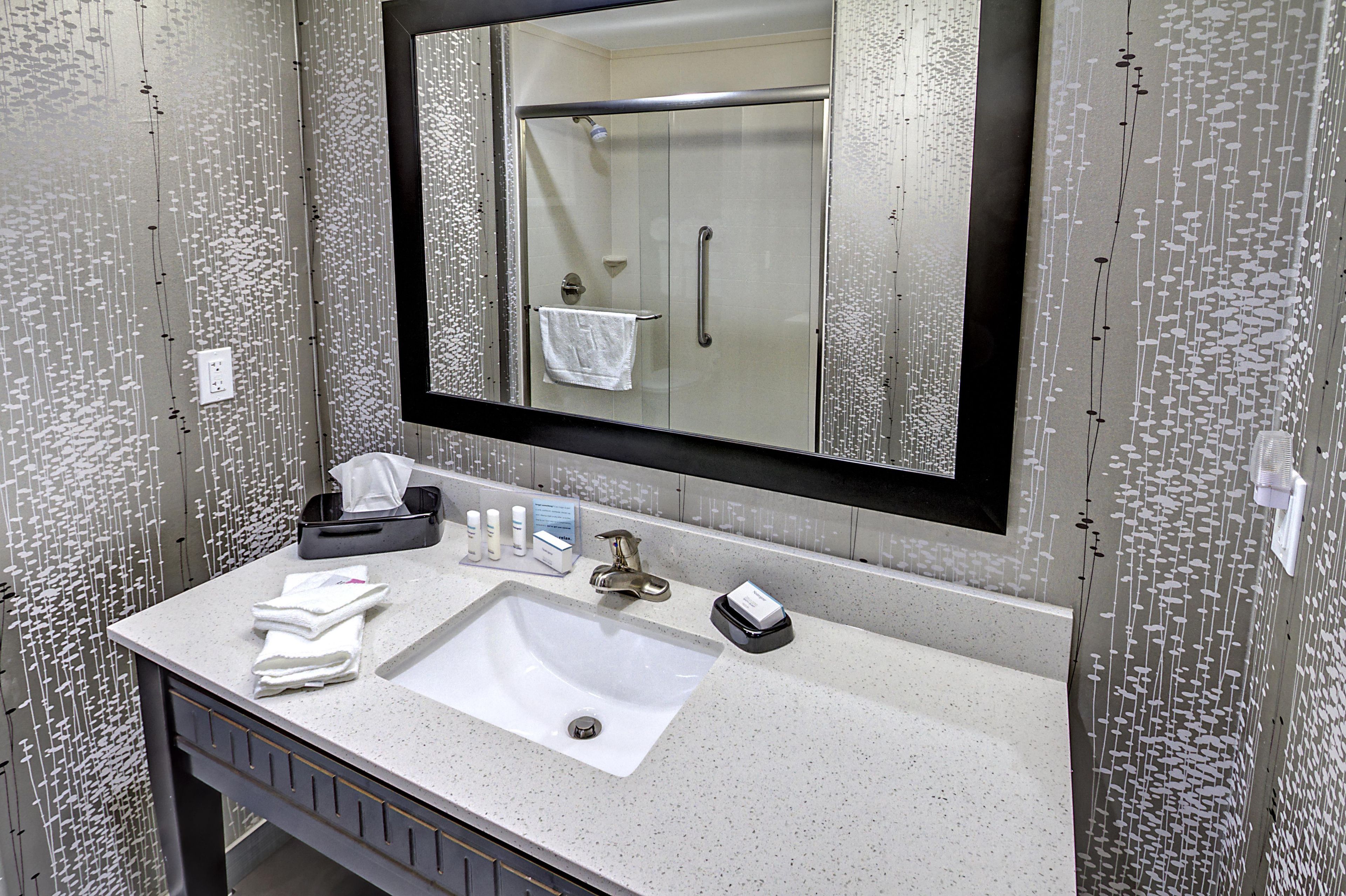 A bathroom with a large mirror, a sink, and a towel rack.