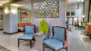 A lobby with two blue upholstered chairs, a green vase, and a wall-mounted mirror. - Hampton Inn & Suites Ada (Ada)