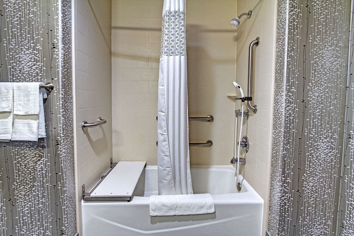 A shower with a white curtain, a handheld showerhead, a handheld shower attachment, and a grab bar.