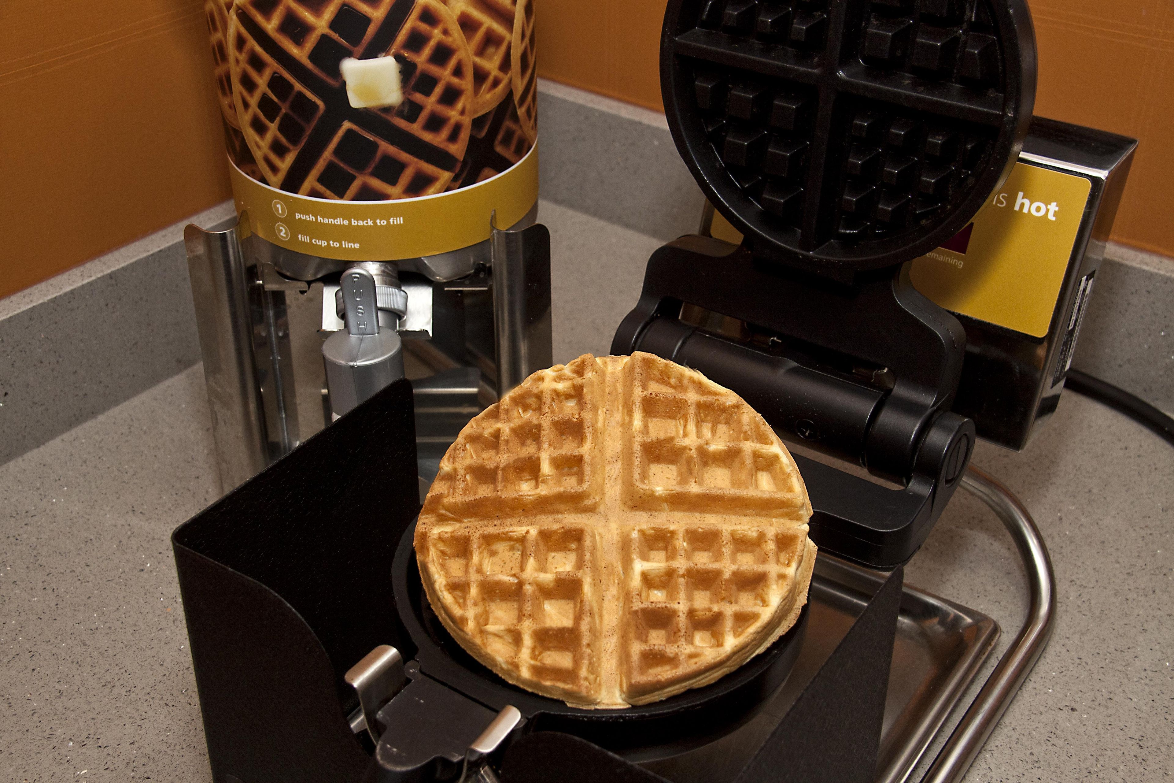 A waffle maker with a waffle inside, a waffle iron, and a hot plate.