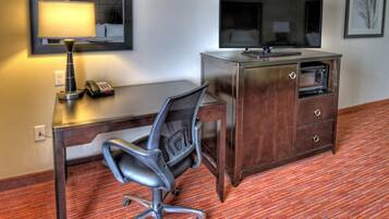 A hotel room with a desk, chair, television, and a minibar.
