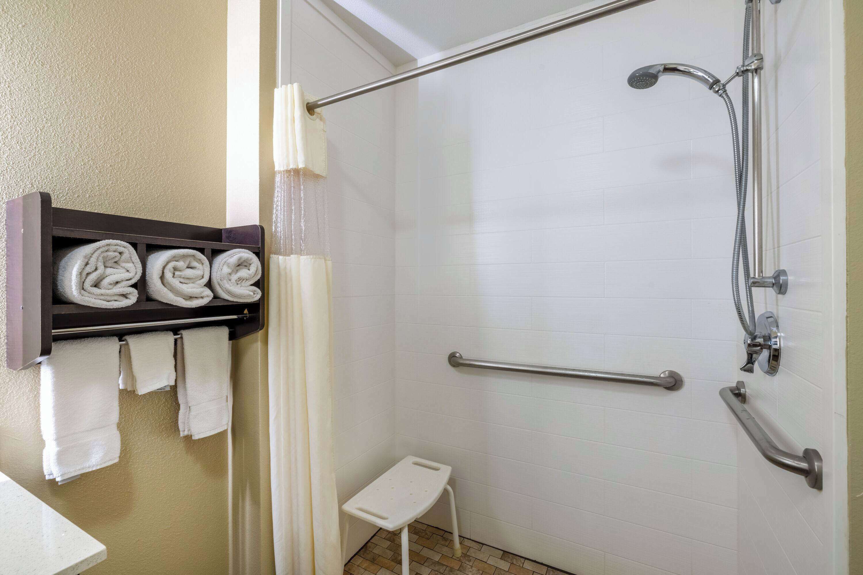 A shower area with a grab bar, a towel rack with folded towels, and a small step stool.