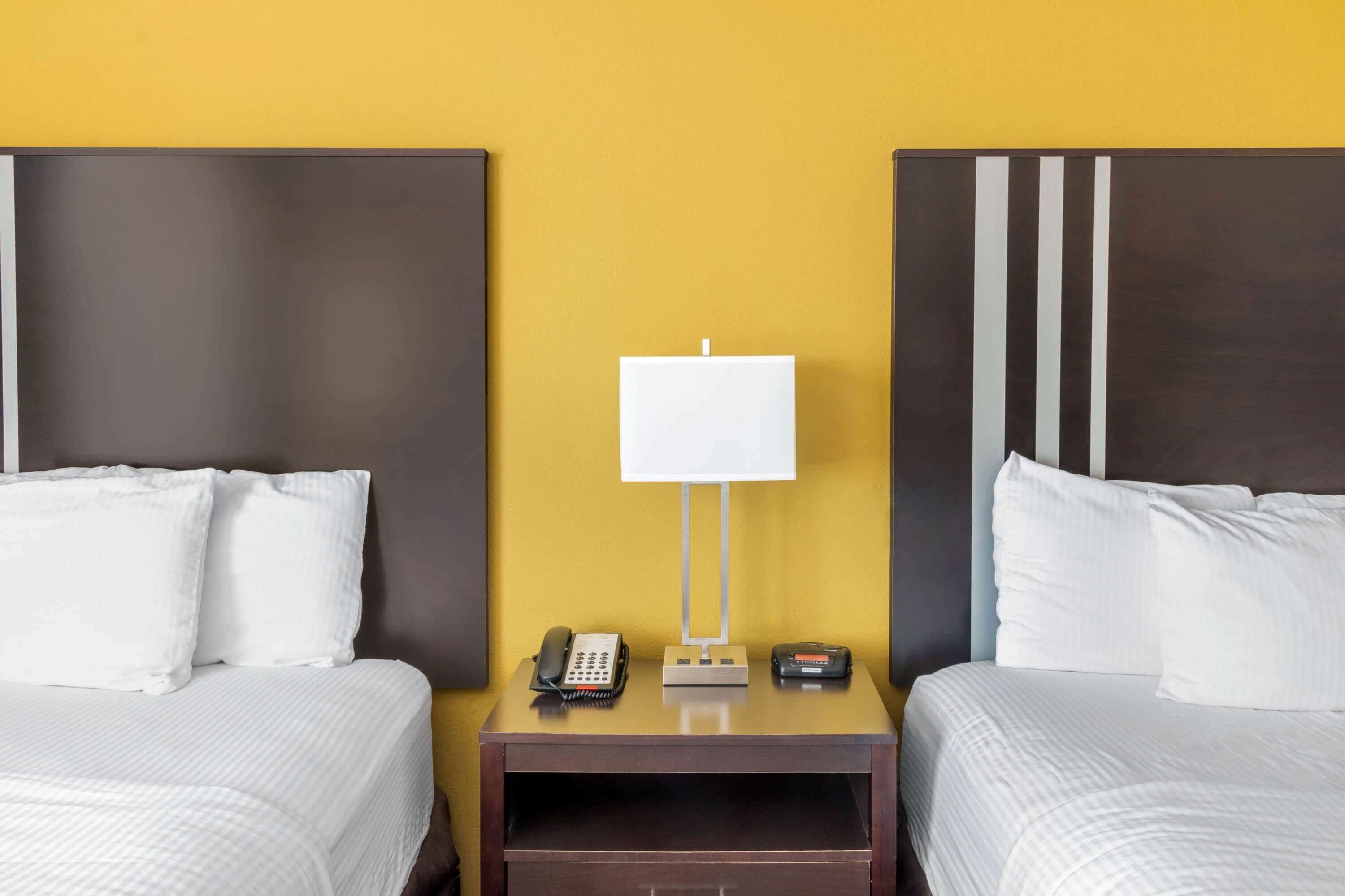 A hotel room with two beds, a nightstand with a lamp, a phone, and a small table.