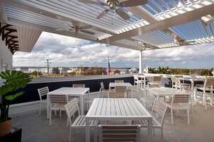 An outdoor patio with white tables and chairs, a ceiling fan, and a view of the cityscape.