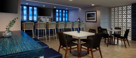 A modern dining area with a bar, multiple seating arrangements, and a view of the kitchen through glass doors.