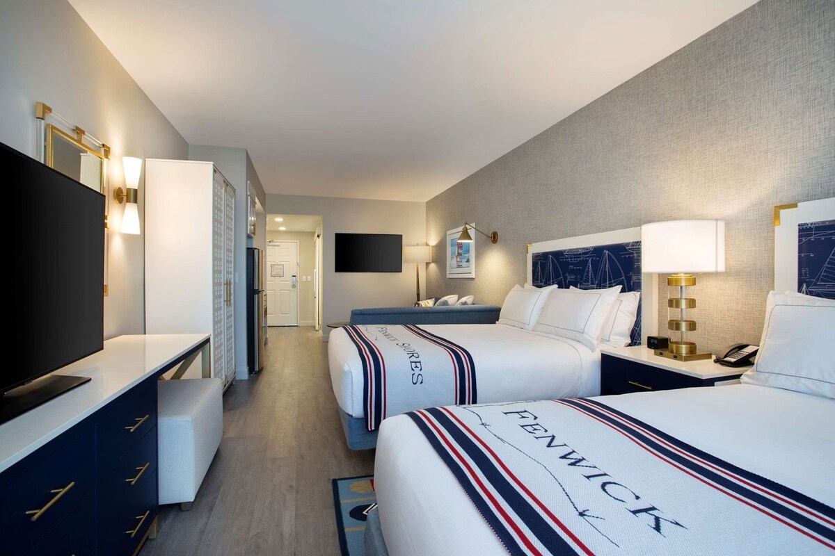 A hotel room with two beds, a TV, a desk, and a mirror.