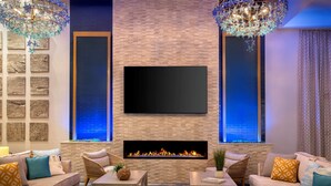Un salon moderne avec une cheminée en briques, un téléviseur à écran plat, des meubles en osier et un éclairage décoratif.