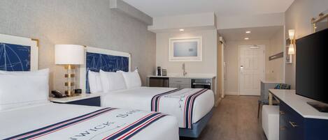 A hotel room with two beds, a desk, a television, and a bathroom.