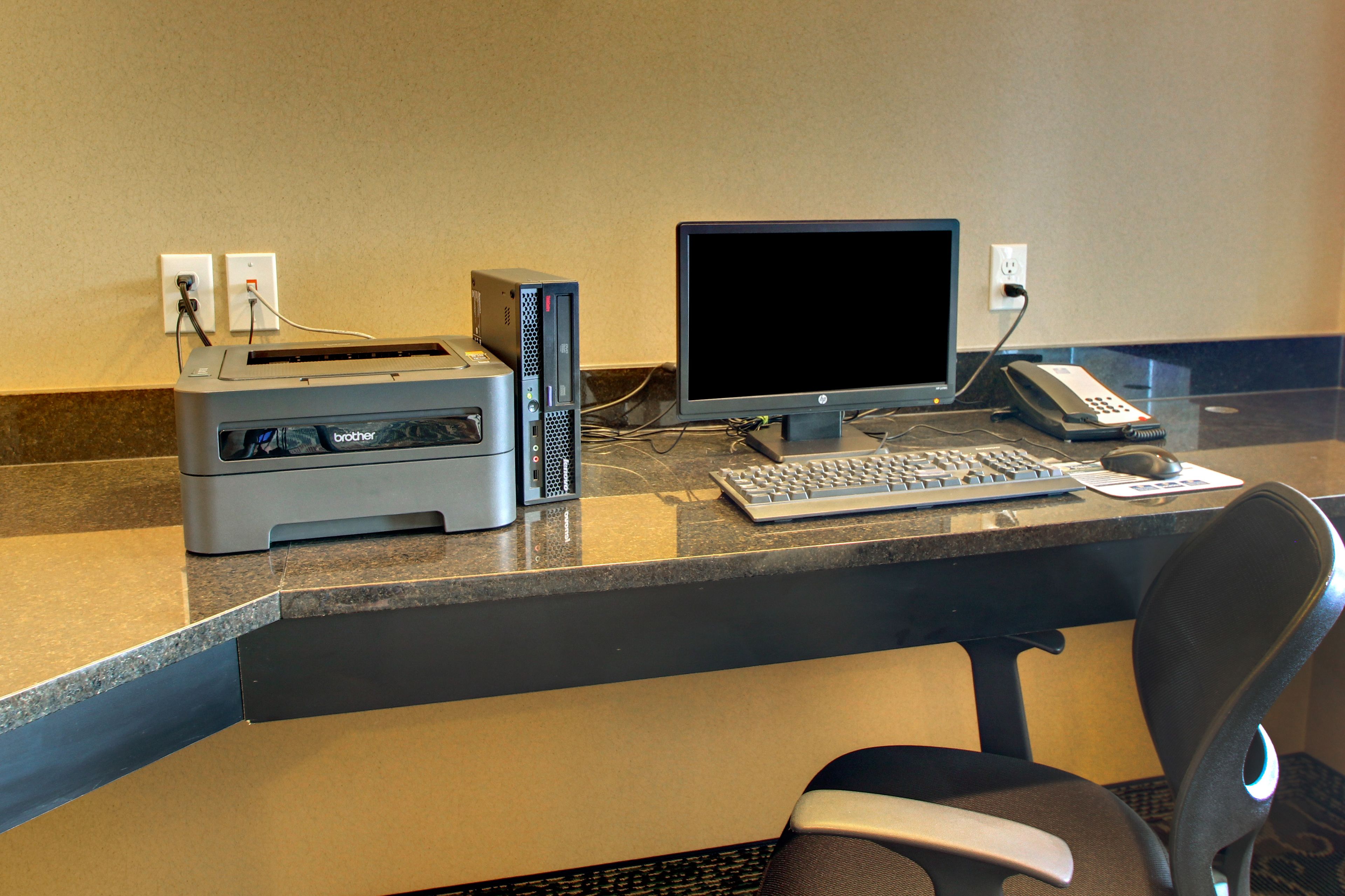 Een hotel receptiebalie met een computer, een printer, een telefoon en een stoel.