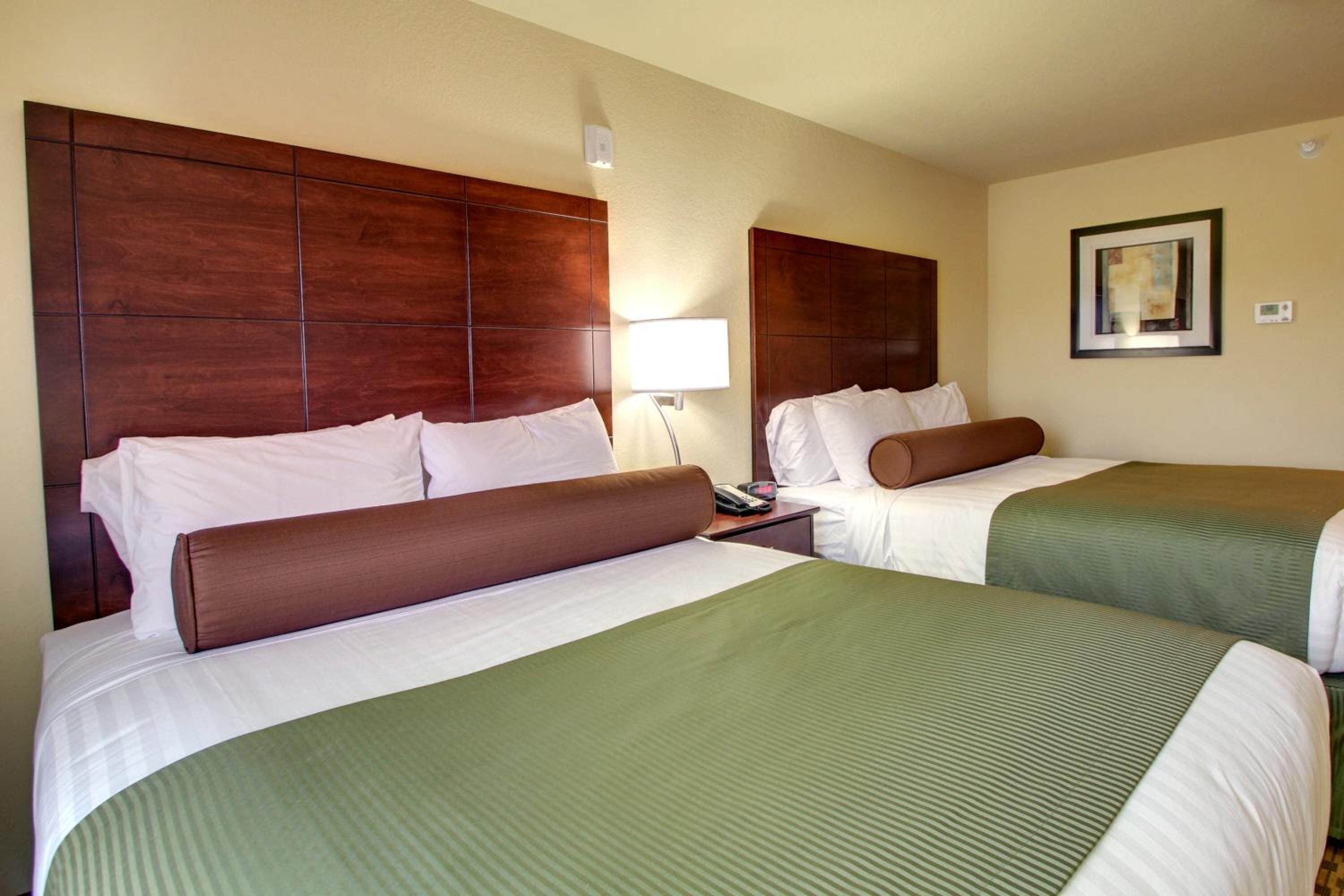 A hotel room with two beds, each with a wooden headboard, a bedside table with a lamp, and a framed picture on the wall.