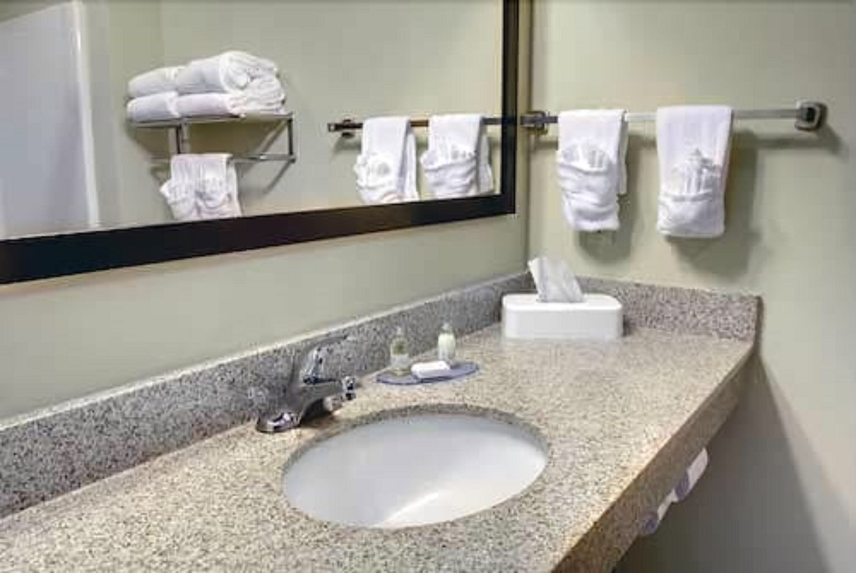A bathroom with a granite countertop, a sink, a mirror, and a towel rack with folded towels.