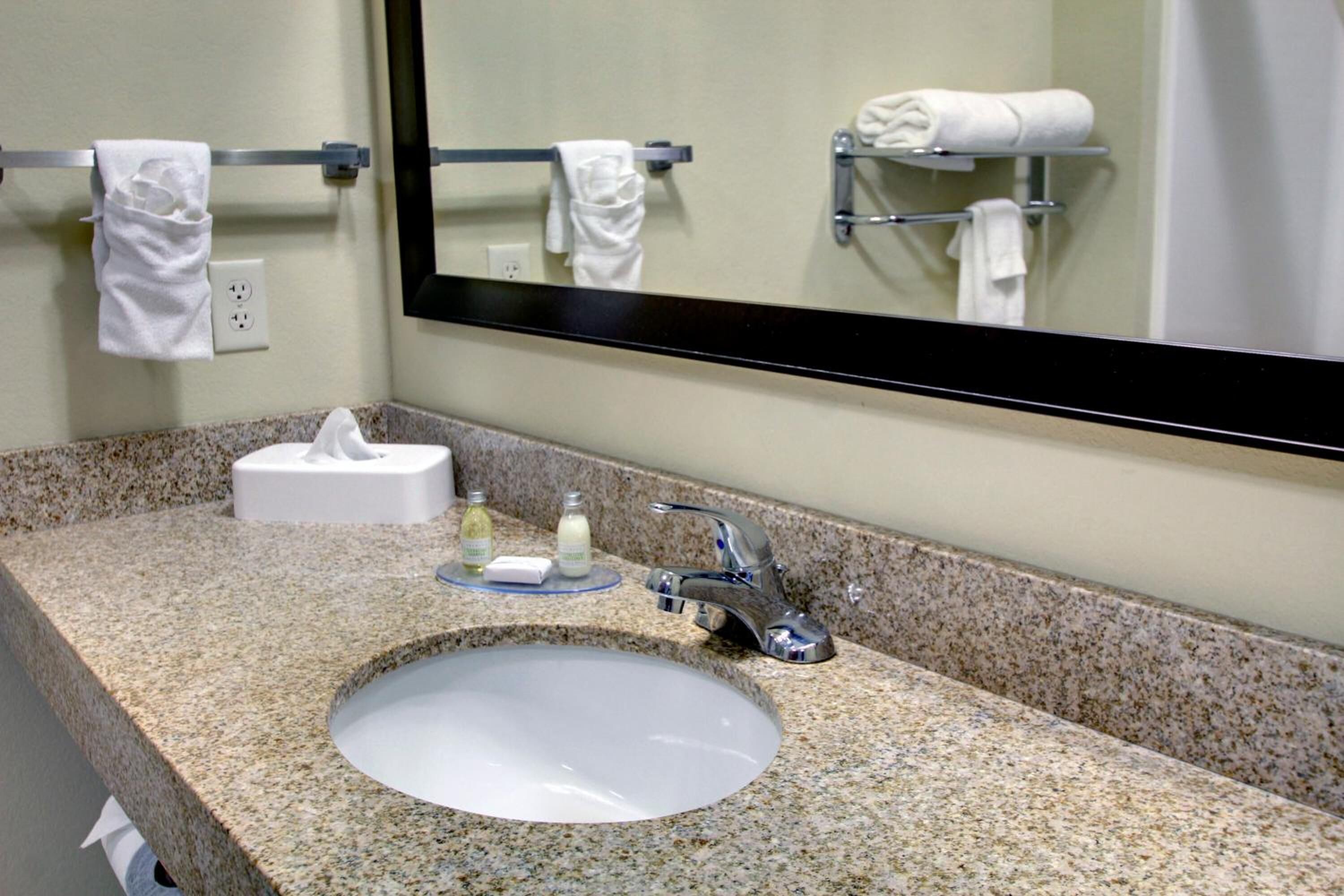 A bathroom with a granite countertop, a sink, a mirror, and a towel rack with towels.