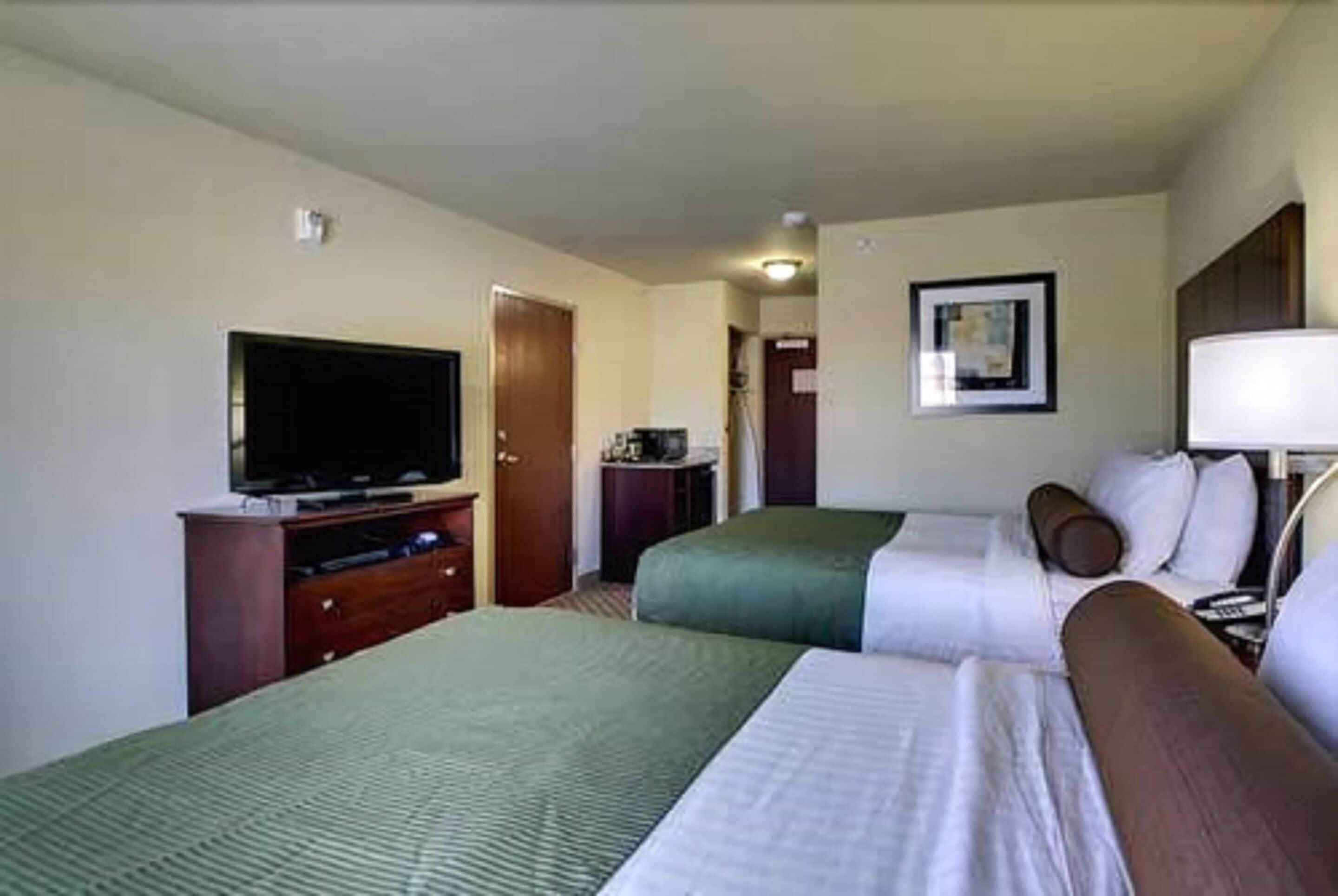 Quarto de hotel com duas camas, televisão, escrivaninha e um quadro pendurado na parede.