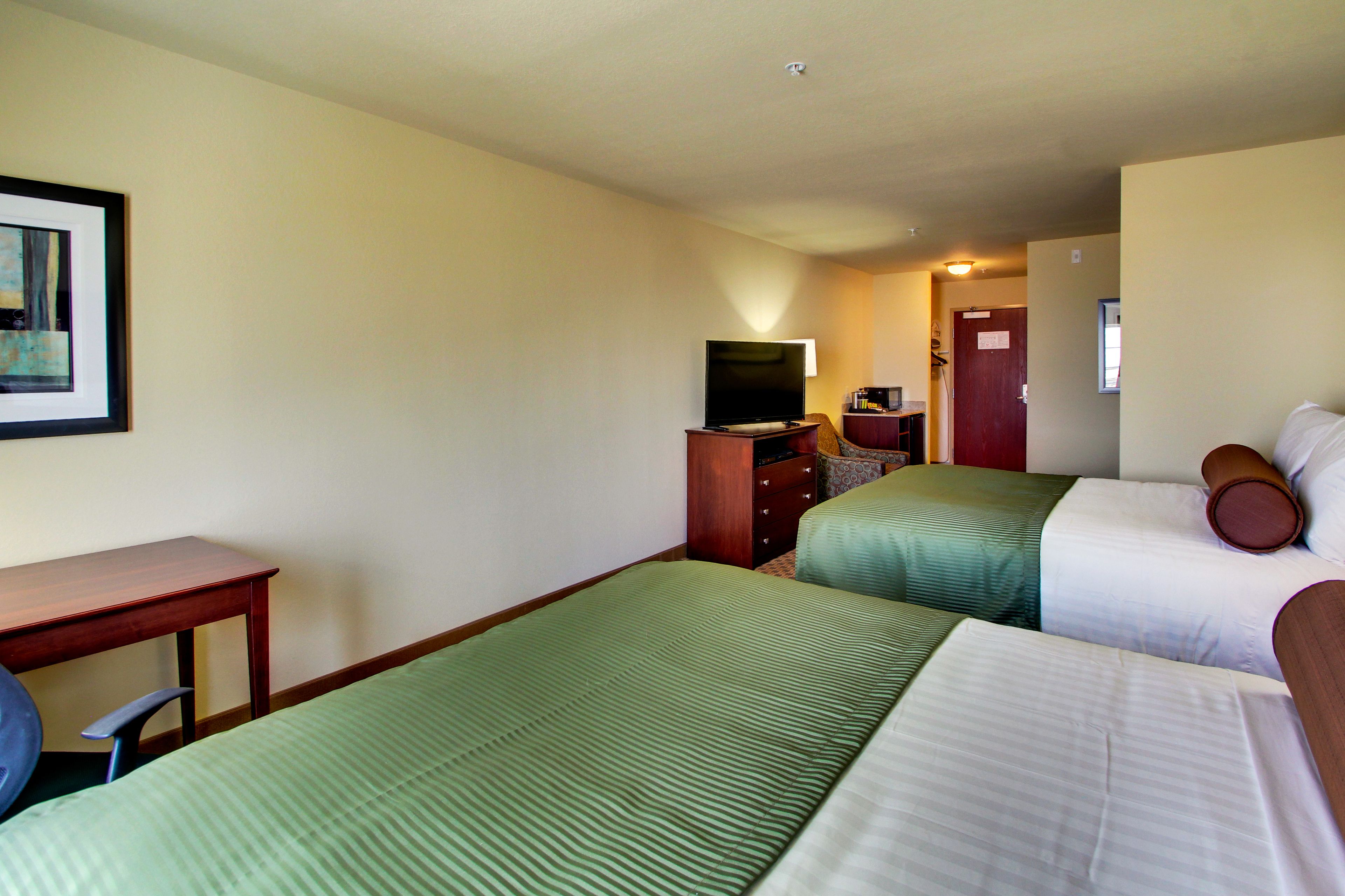 A hotel room with two beds, a desk, a television, and a door leading to another room.