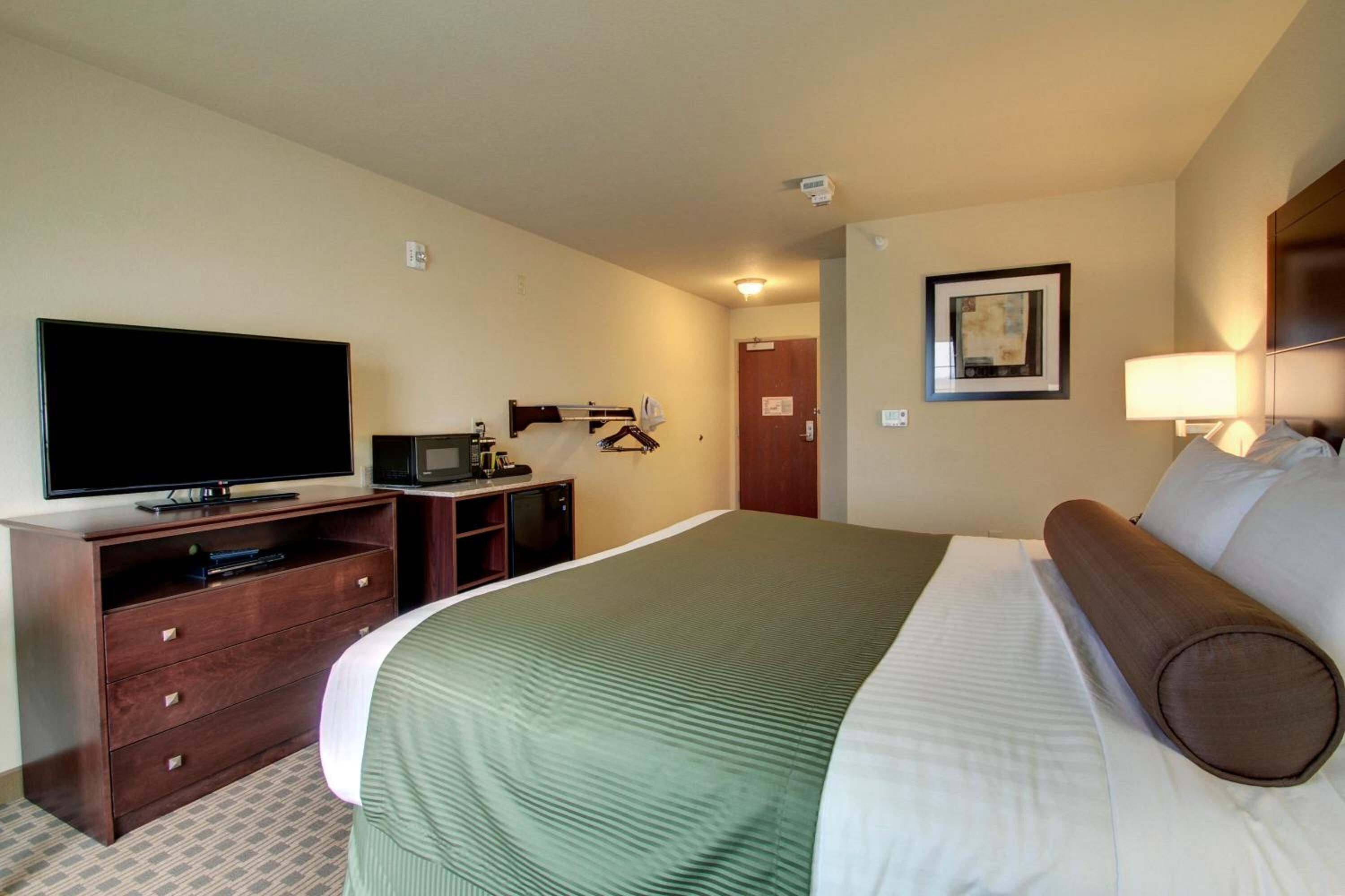 A hotel room with a bed, a television, a dresser, a desk, and a door.