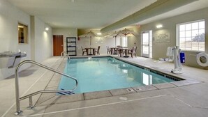 Una piscina interior con trampolín, sillas de descanso y una sombrilla.