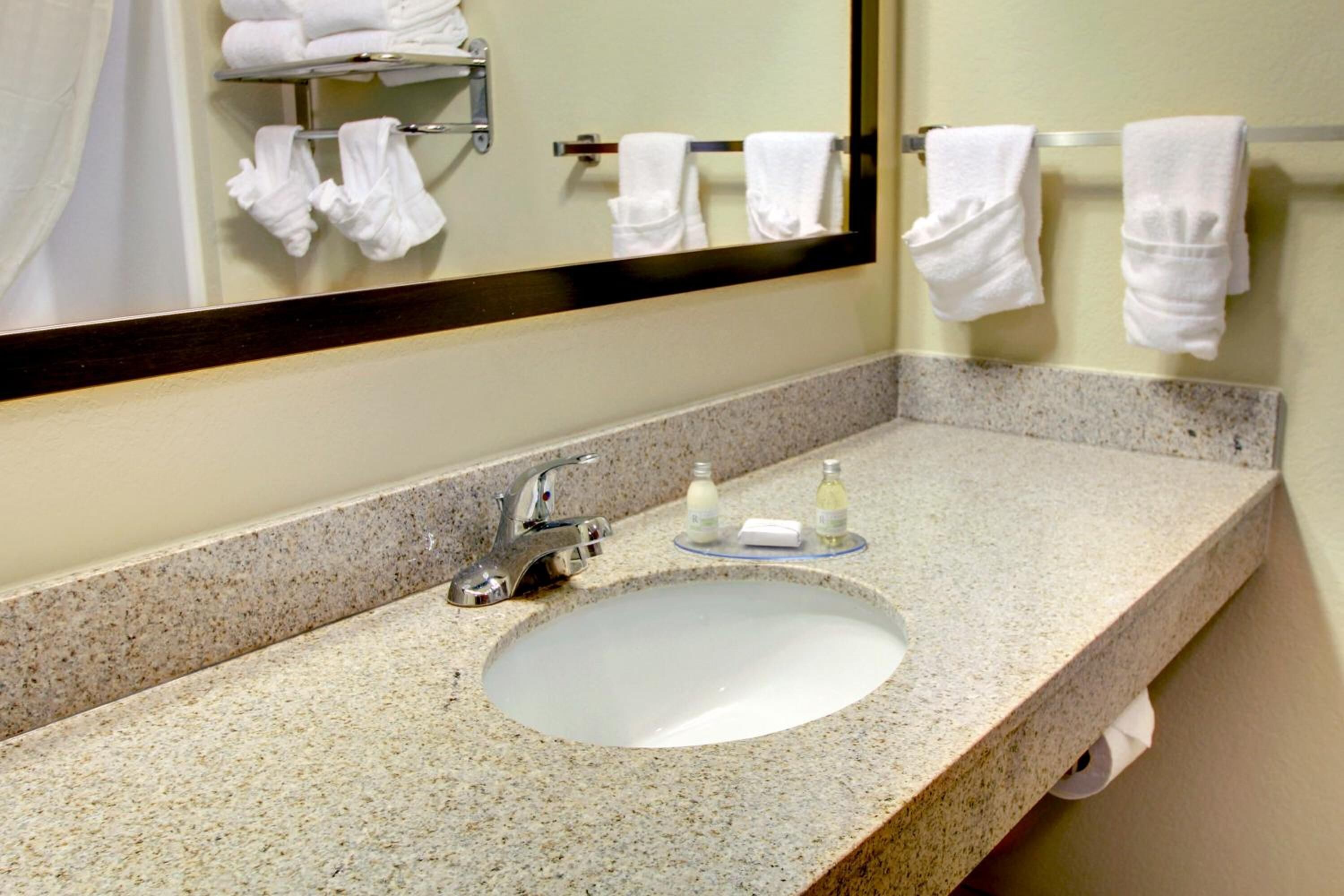 A bathroom with a granite countertop, a sink, a mirror, and a towel rack with towels.