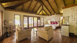 Una habitación amplia con pisos de madera, una cama con dosel, dos sofás, una mesita y un refrigerador.
