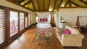 Una habitación amplia con techo de madera, una cama con dosel, una mesa de centro de vidrio y un sofá.