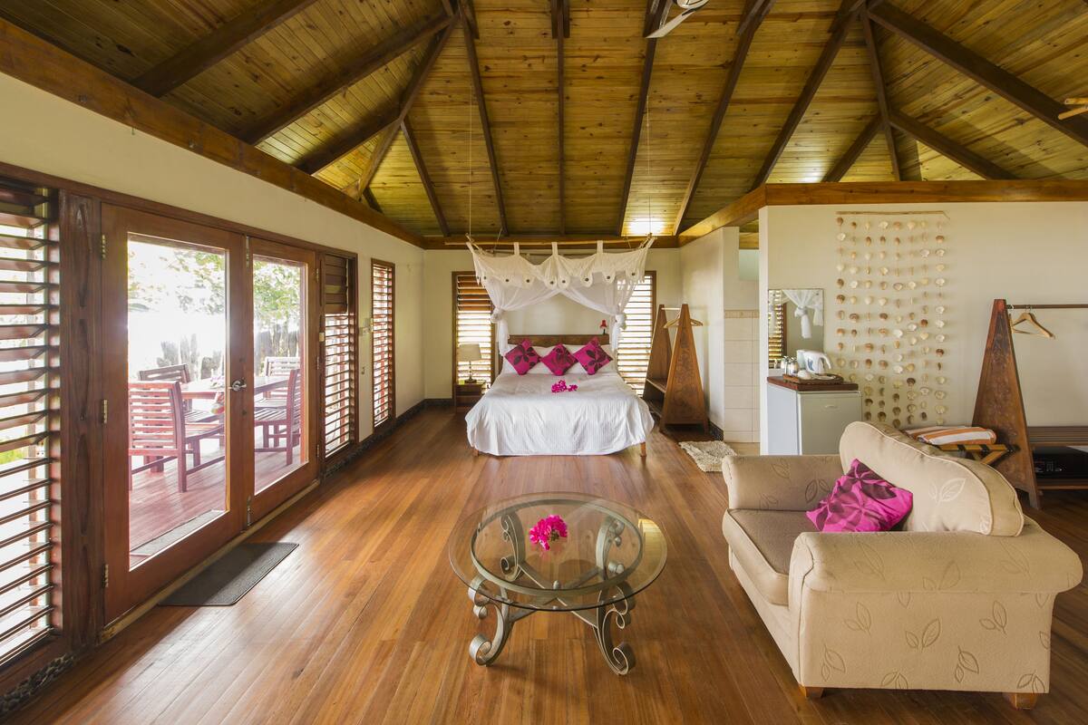 A spacious room with a wooden ceiling, a bed with a canopy, a glass coffee table, and a sofa.