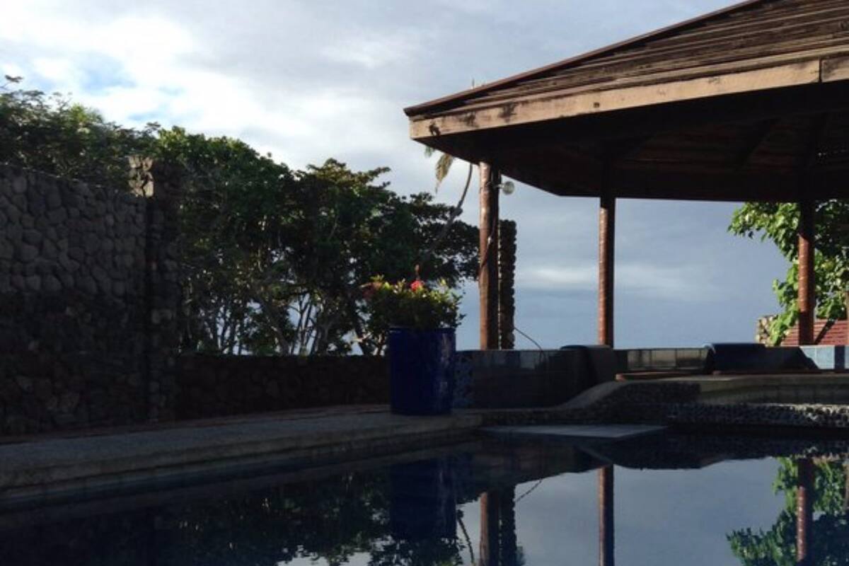 A swimming pool with a stone wall and a wooden structure reflecting in the water.