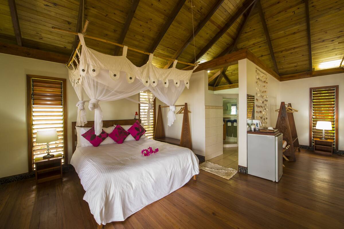 A spacious bedroom with a large bed, wooden flooring, a canopy bed, and a small kitchenette.