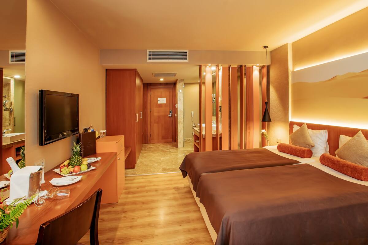 Ein Hotelzimmer mit Schreibtisch, zwei Betten, einem Fernseher und einem durch eine offene Tür einsehbaren Badezimmer.