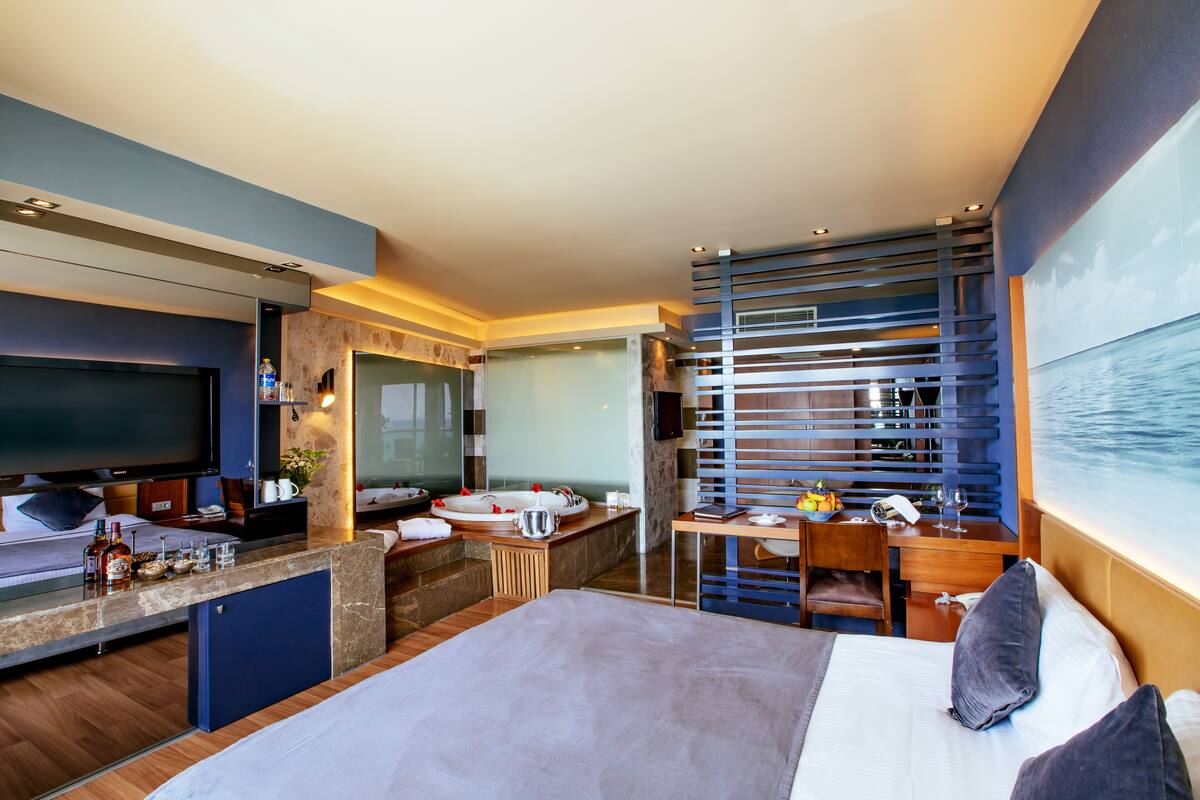 Ein modernes Hotelzimmer mit einem großen Bett, einem Schreibtisch mit Computer, einem Fernseher und einer Sitzecke mit Meerblick.