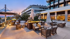 A rooftop terrace with wicker furniture, umbrellas, and a view of a modern building.