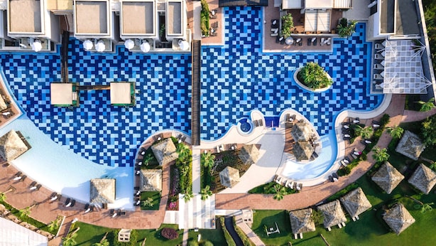 An aerial view of a resort with a large pool area, multiple lounge areas, and a well-maintained garden.