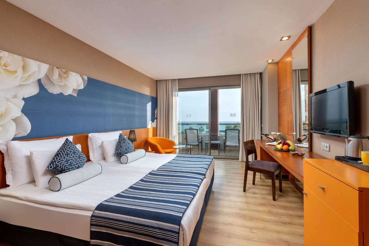Ein Hotelzimmer mit einem großen Bett, einem Schreibtisch mit Fernseher und einem Balkon mit Blick.