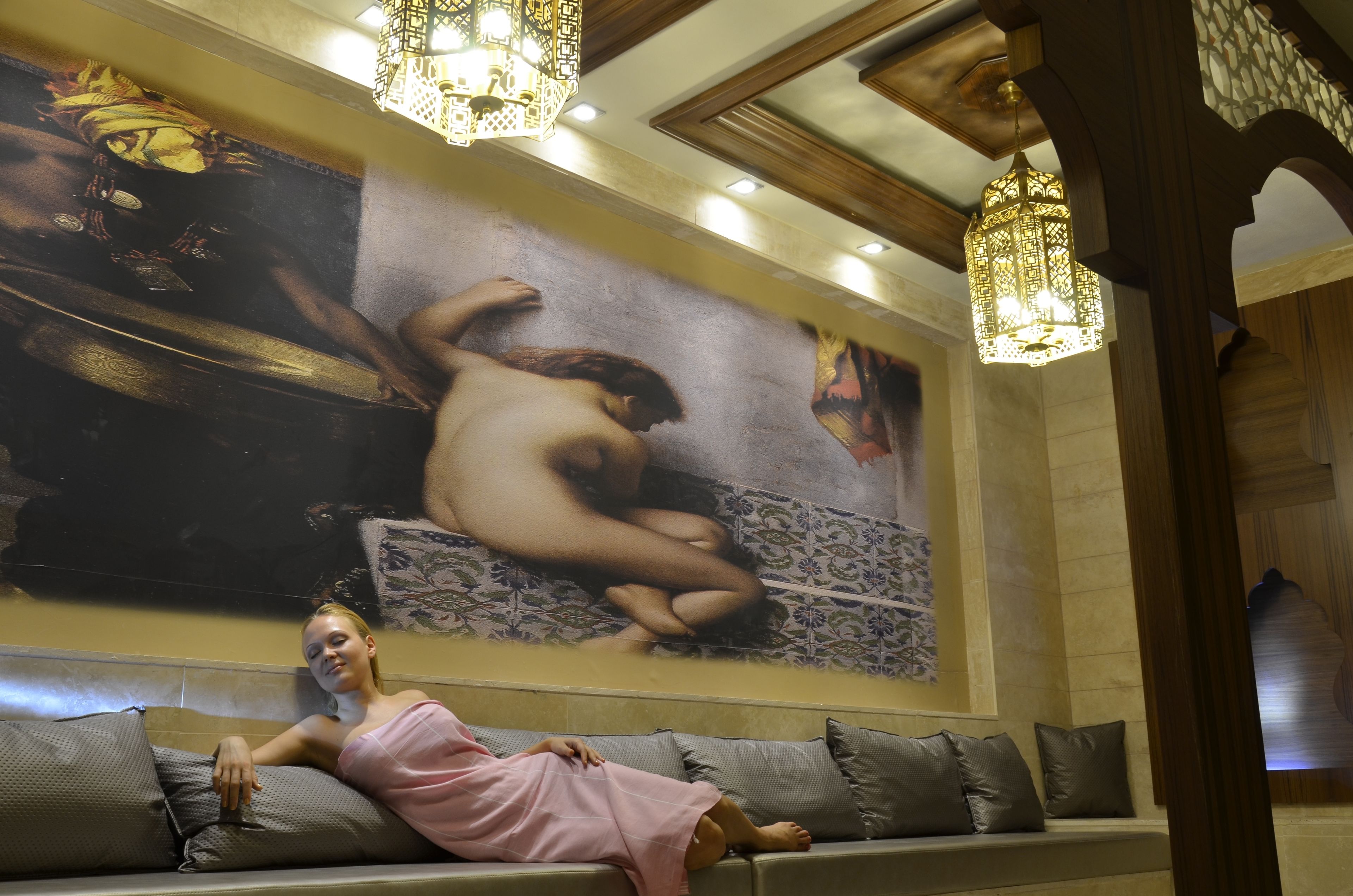 A woman in a pink robe sitting on a sofa with a large mural in the background.