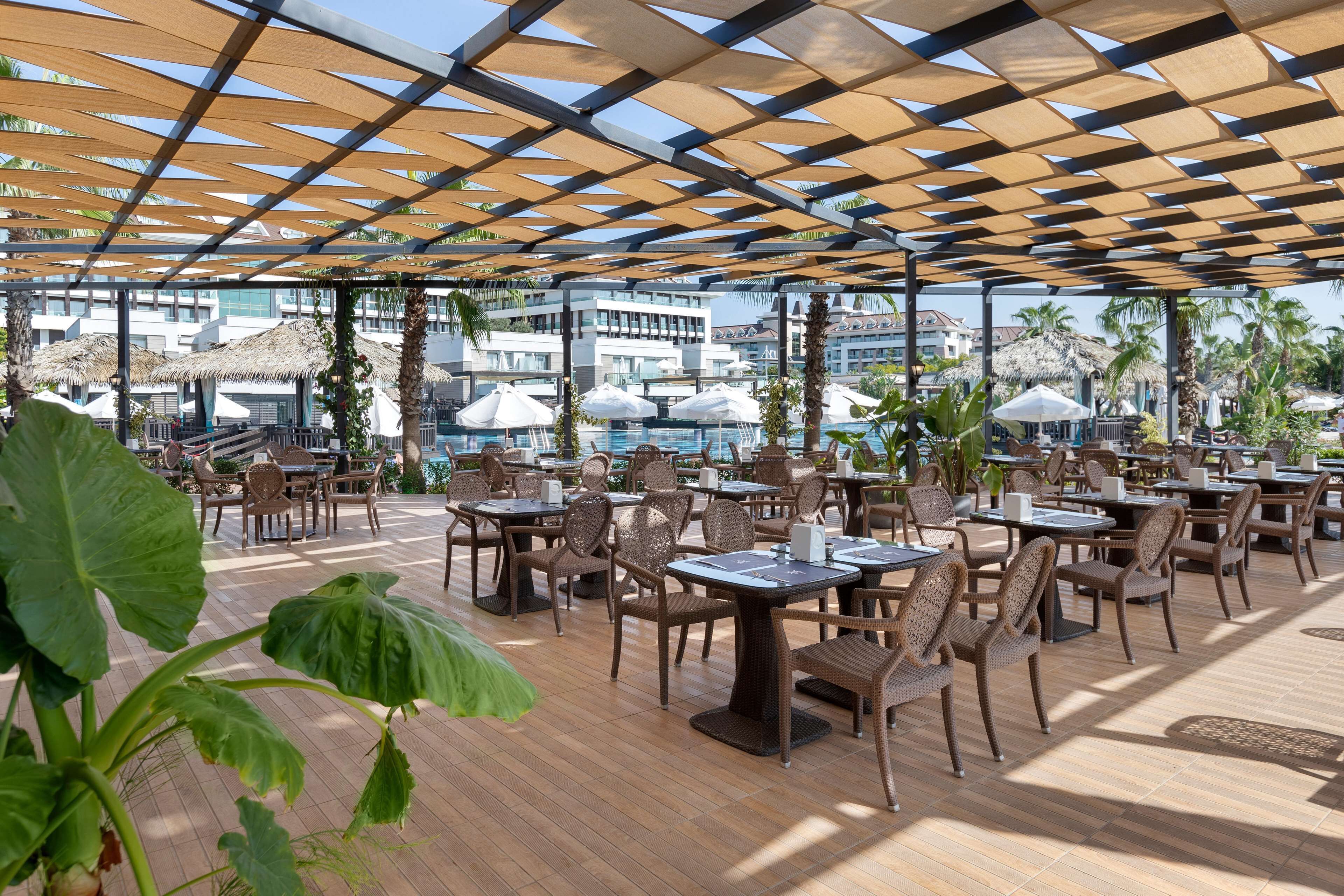 Un espace de restauration en plein air, avec des tables et des chaises, des parasols et une vue sur les bâtiments du complexe.