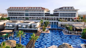 A hotel with a large pool area, multiple balconies, and a view of the surrounding landscape.