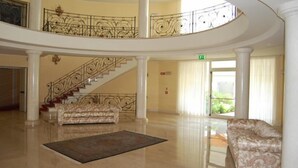 Un hall d’entrée spacieux, agrémenté d’un grand escalier, d’un canapé à motifs et d’une grande fenêtre offrant une vue sur la verdure.