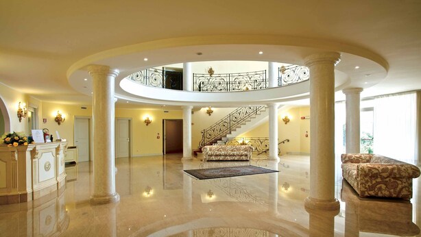 Un hall d’entrée spacieux avec un escalier central, un comptoir d’accueil et un canapé à motifs.