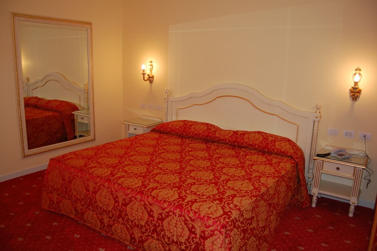 A hotel room with a large bed, two bedside tables, a nightstand, and a mirror.