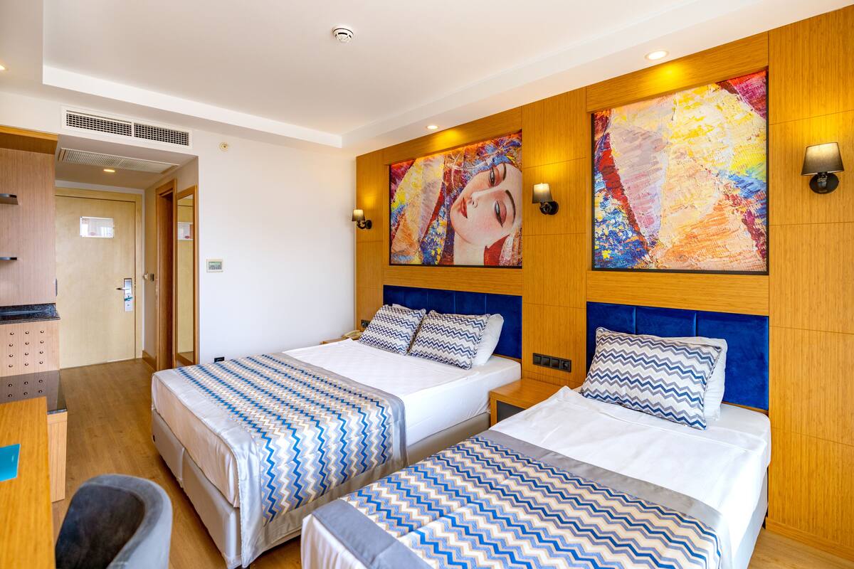 Een hotelkamer met twee bedden, een bureau en een stoel. Er hangen twee schilderijen aan de muur en staan twee wandlampen.